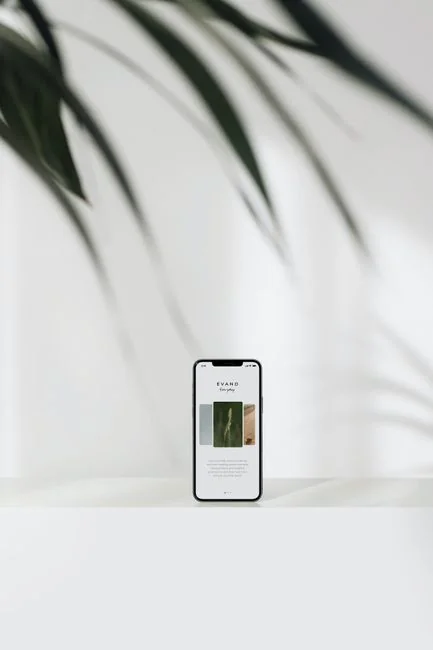 Main tenant un smartphone affichant l’interface d’une application de portefeuille numérique, avec un écran d’ordinateur flou à l’arrière-plan.